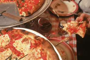 A vintage photograph of two margarita pizzas with slices cut out on a table with a red and white checkered tablecloth