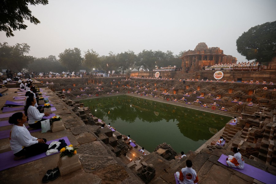 People practice yoga on stepped terraces around a pool of water.