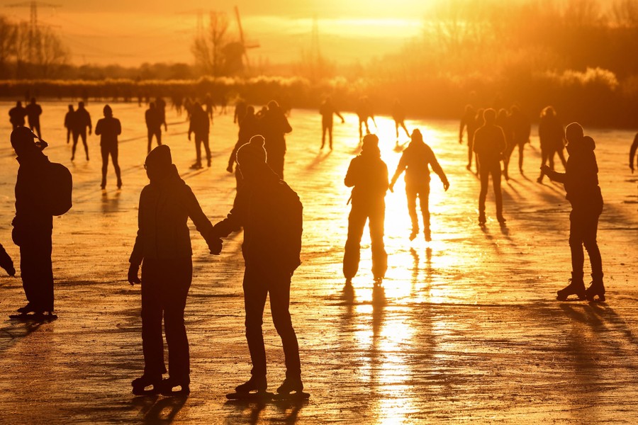 Dozens of people skate on a broad frozen surface at sunset.