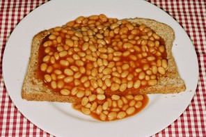 Photograph of baked beans on toast. The toast is on a white plate atop of red-and-white gingham tablecloth.