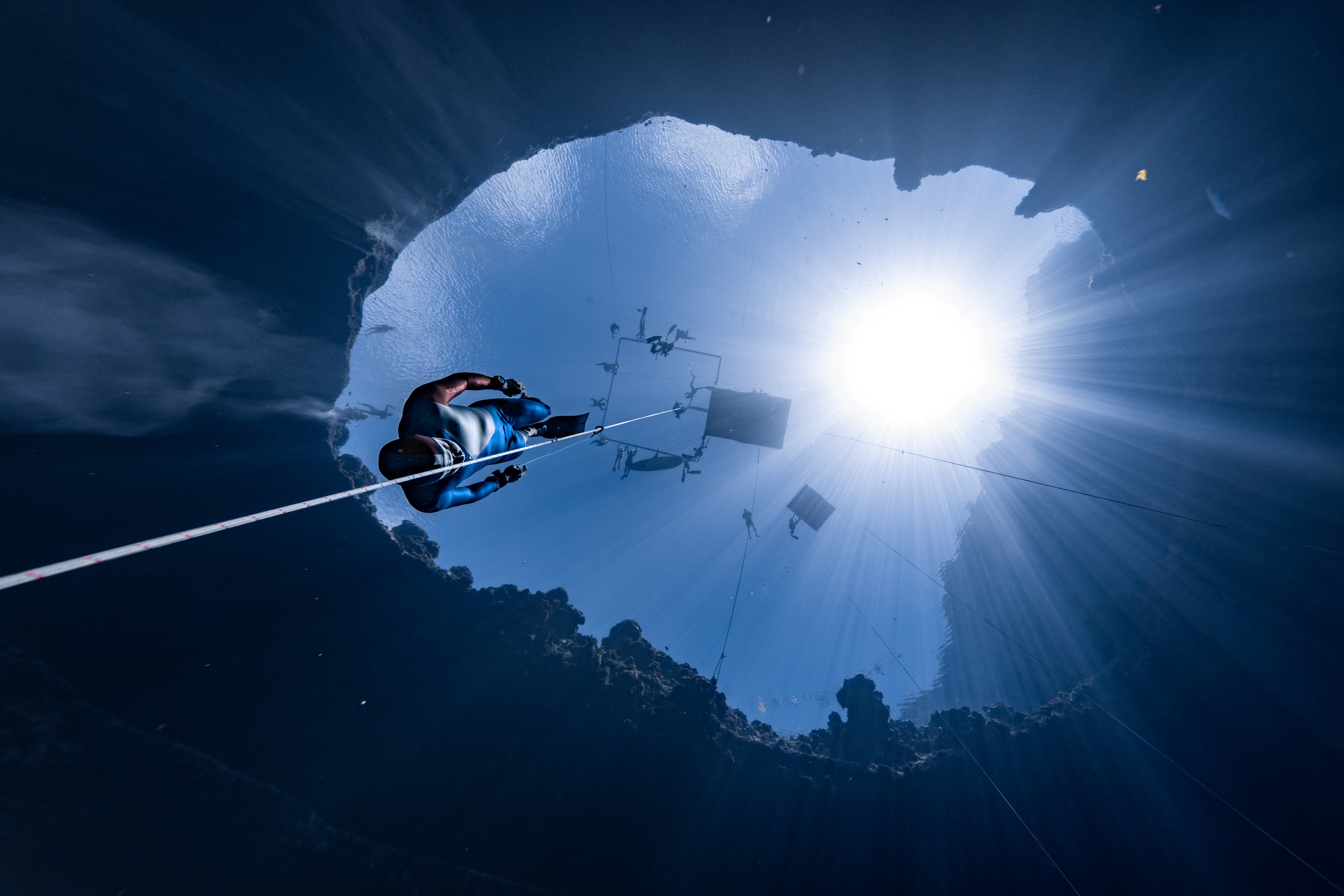 A freediver descends deep underwater into a sinkhole.