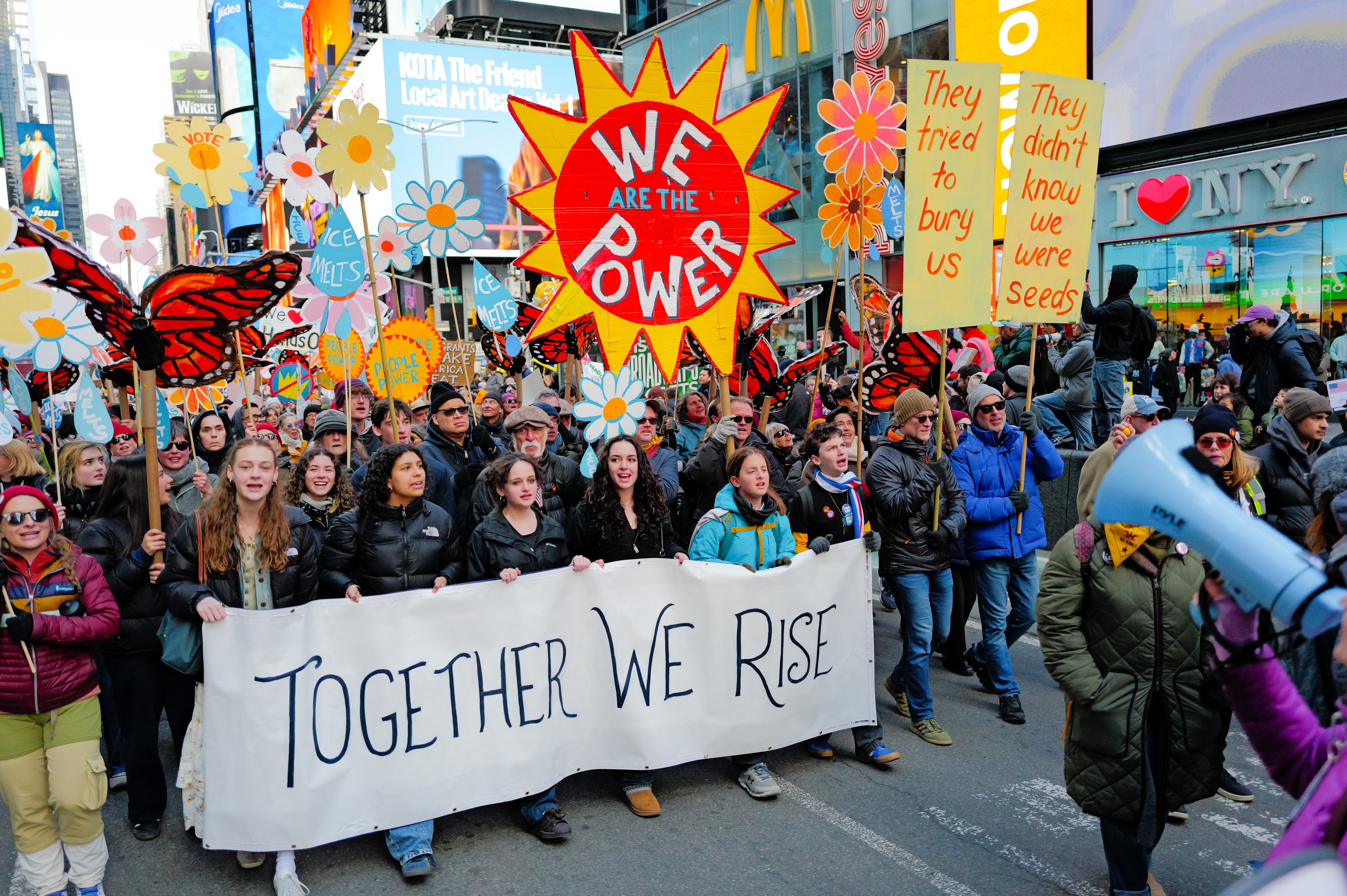 Protesters march behind a banner that reads 'together we rise' and beneath a sign that reads 'we are the power.'