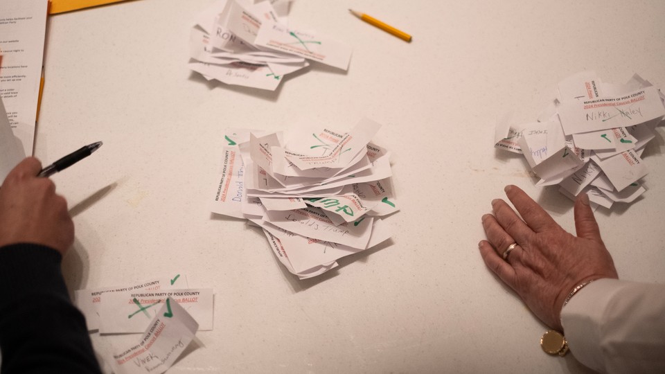 Hands on a desk with ballot slips during the 2024 Iowa Republican caucuses