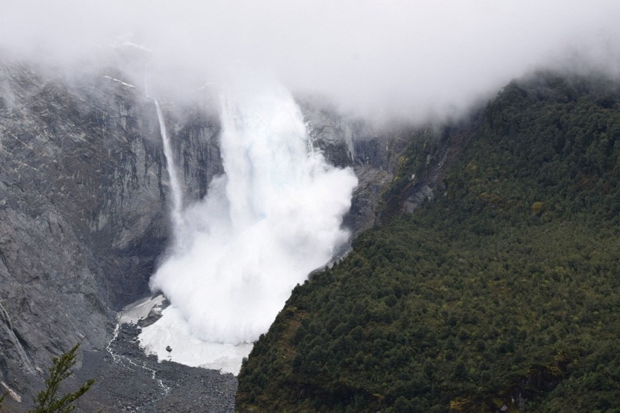 Large amounts of ice cascade down a cliff, falling to a river valley below.