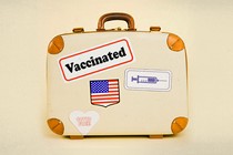 A suitcase with four stickers. One features a syringe, one is a U.S. flag, one says "Vaccinated," and another says "COVID Free."