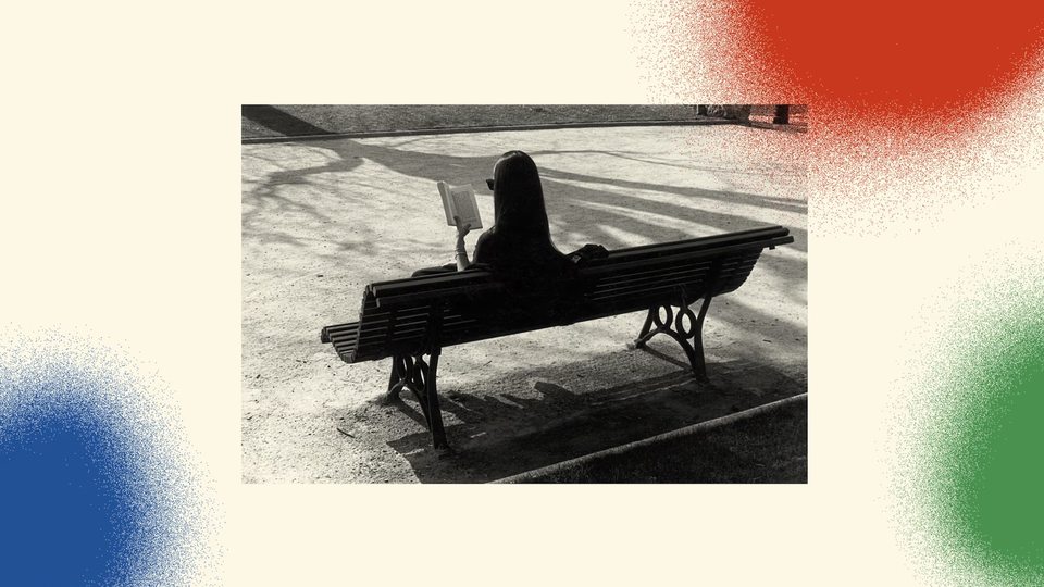 A black-and-white photo features a woman sitting on a park bench with her back to the camera. She is reading a book, and on the ground, the shadow of a tree is stretching toward her. The photo is set against a background with three spray-painted circles. In the bottom-left corner is a blue one, in the bottom-right corner is a green one, and in the top-right corner is a red one.