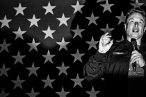 Photo of Elon Musk speaking in front of an American flag