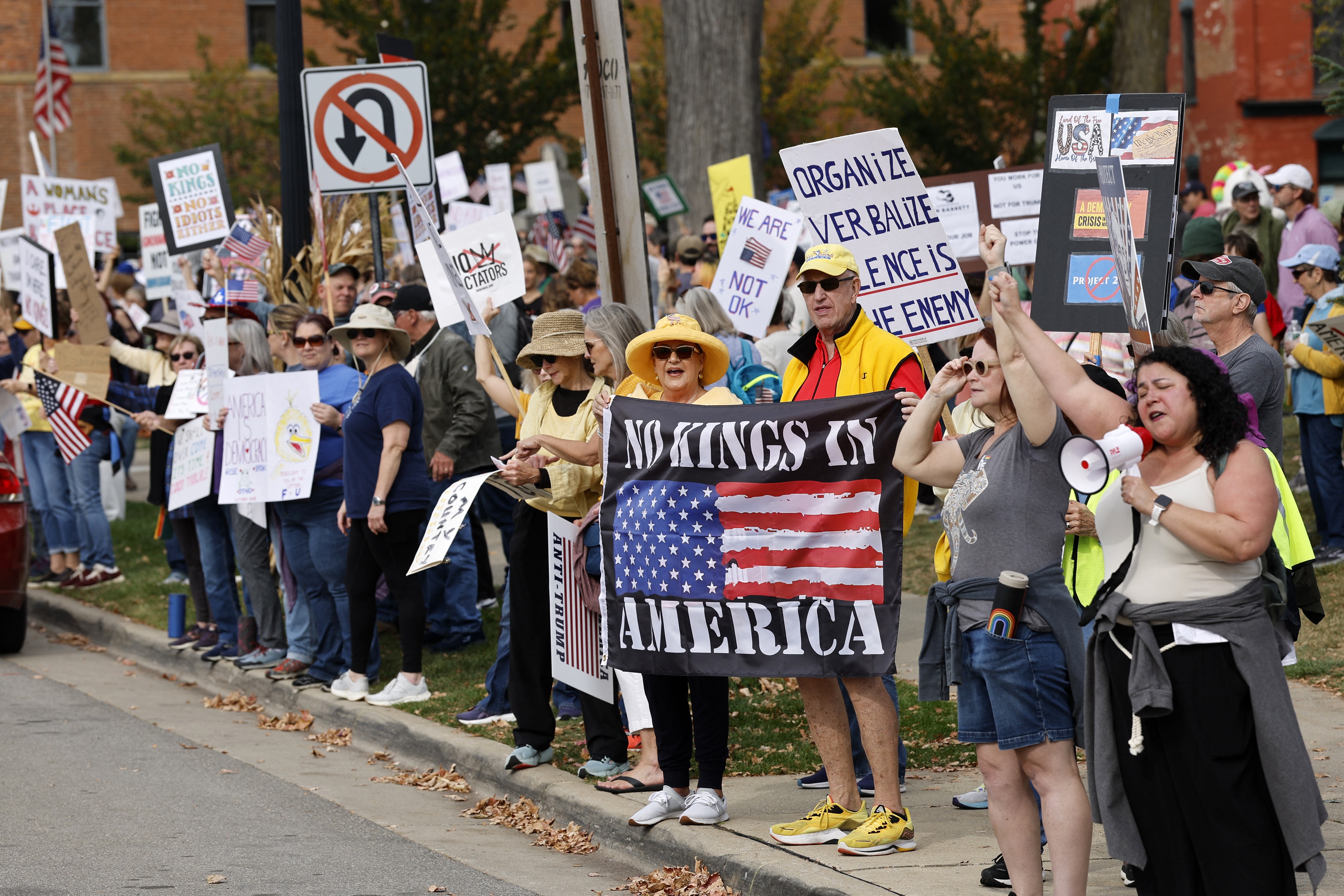 Protesters in a Michigan town stand along a sidewalk holding signs.