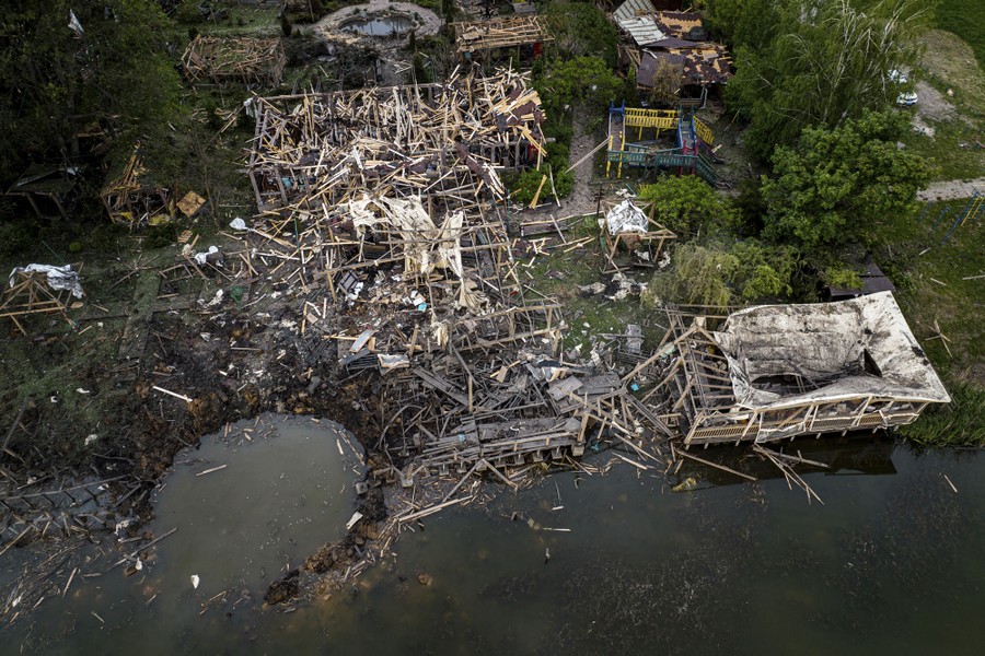 A crater and wreckage of destroyed lakeside buildings, part of a small resort compound, seen from above