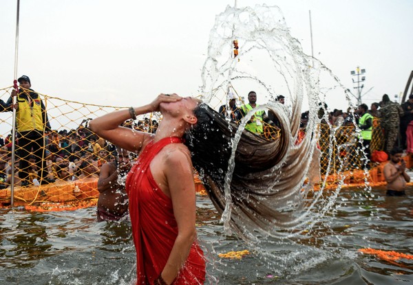 A person holds their nose while flipping their long, wet hair back after dunking in shallow water.