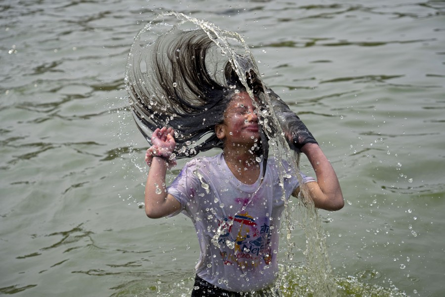 A person stands in knee-deep water, whipping their long wet hair over their head.