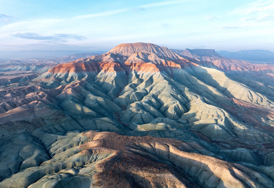An aerial view of a deeply eroded mountain, exposing many colorful layers of stone