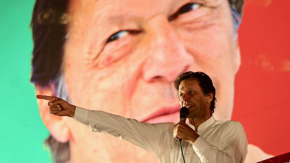 Imran Khan holds a microphone while standing in front of a backdrop with a photograph of his face at a campaign rally
