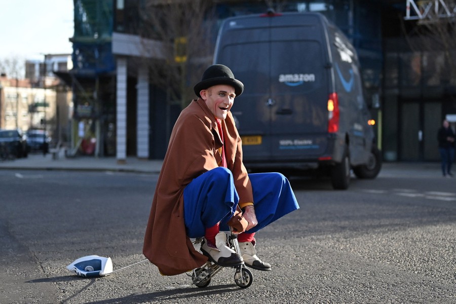 A man dressed as a clown rides an extremely tiny bicycle in a city street.
