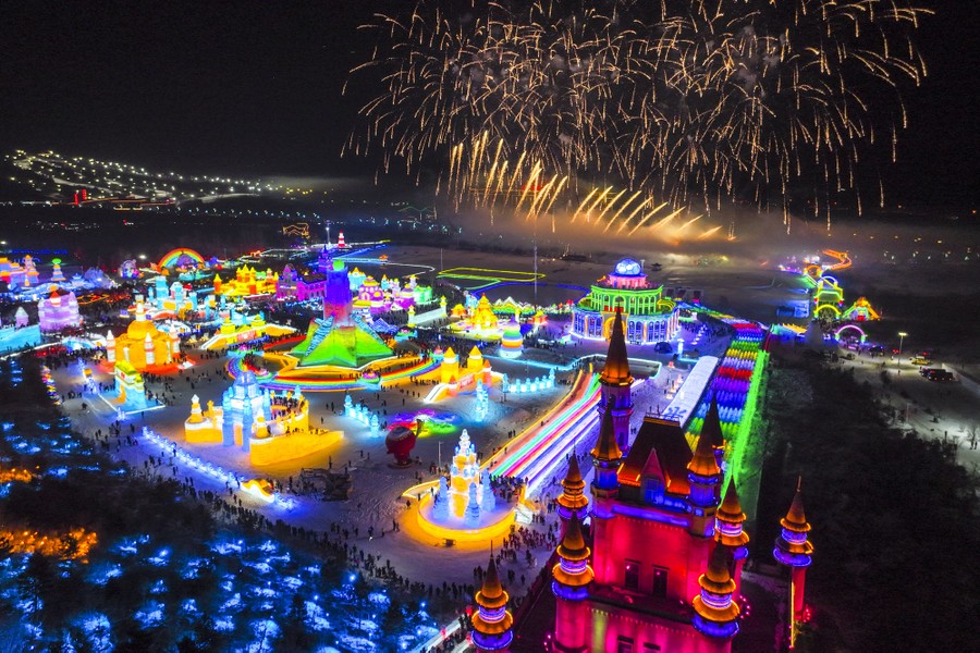 Fireworks explode over illuminated ice sculptures, captured by a drone.