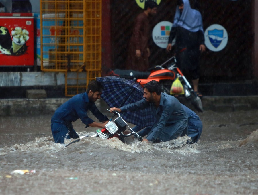 Two people struggle with a motorbike in a flooded street.