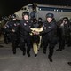 A prisoner with his head pushed down is escorted from a plane by a large group of security forces