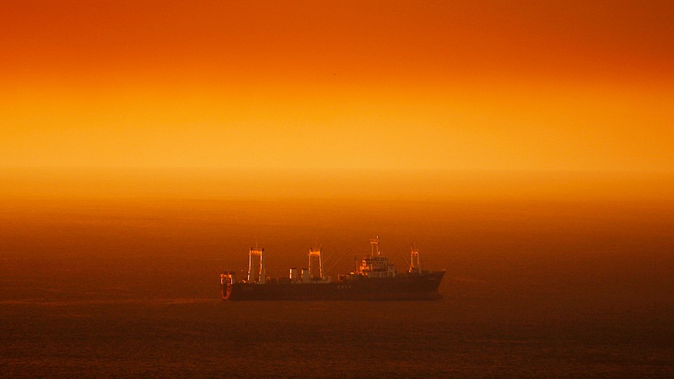 A large ship travels across a stretch of ocean that appears red in the sunlight
