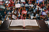 A photo-illustration of an open Bible on a lectern facing a sign-holding crowd at a Trump rally