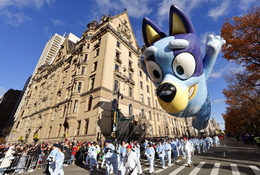 People hold lines during a parade, guiding a huge balloon of the cartoon character Bluey.