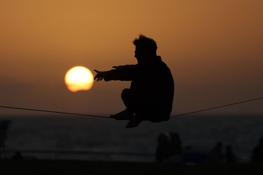 A man is silhouetted against the setting sun as he balances on a line at a beach.