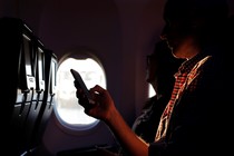 A person holds a phone while being backlit through an airplane window