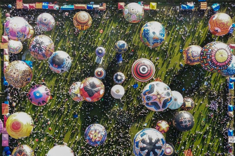 An aerial image shows many hot-air balloons and a large crowd of visitors at a festival.