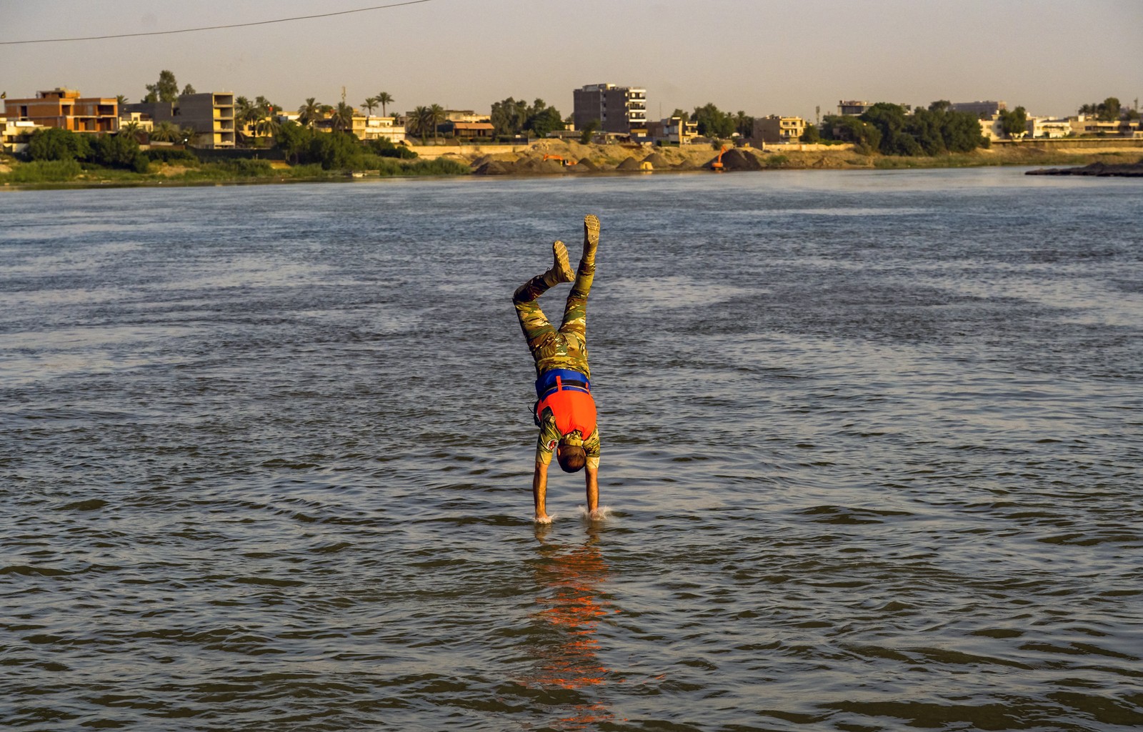 A soldier dives headfirst into a river, their hands just reaching its surface.
