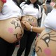 Pregnant women paint smiling faces on their bellies.