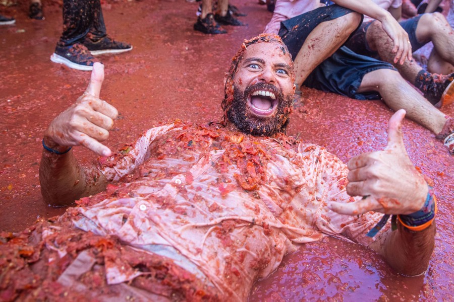 A man smiles and gestures while lying in a huge puddle of tomato pulp.