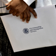 Photograph of hands holding a U.S. flag and an envelope labeled “U.S. Citizenship and Immigration Services”