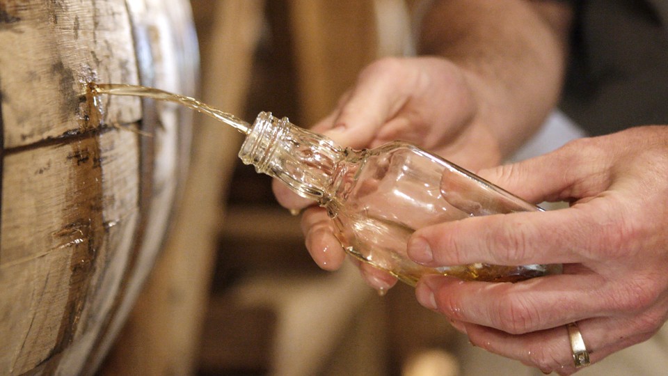 A person holds a bottle to a tapped barrel of whiskey.