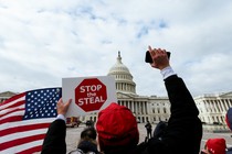 A photo of a man holding a "Stop the Steal" sign in front of the Capitol.