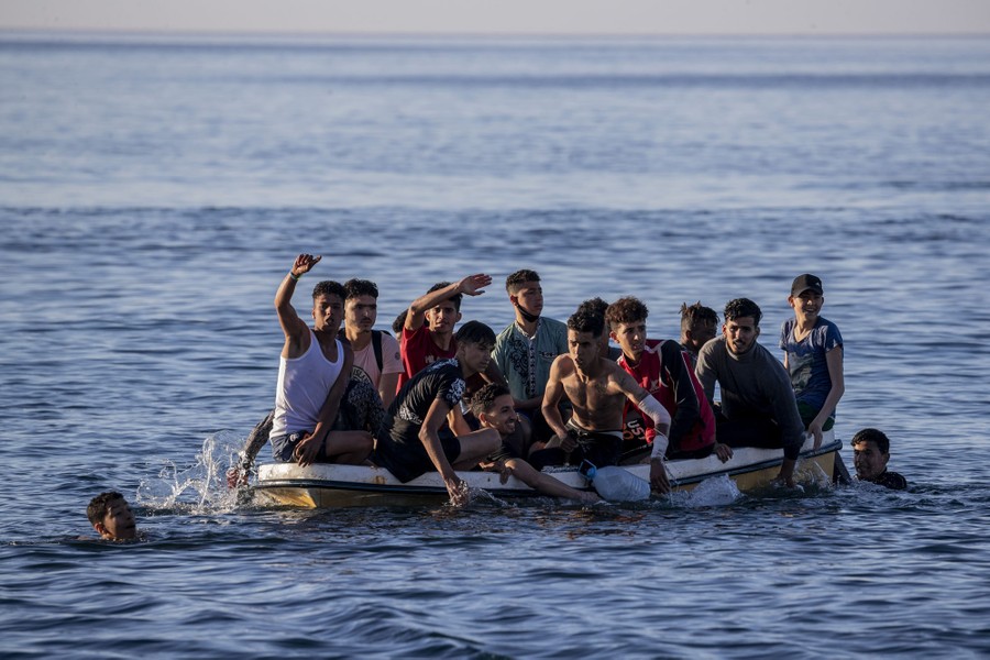 More than a dozen migrants approach a beach in a small boat.