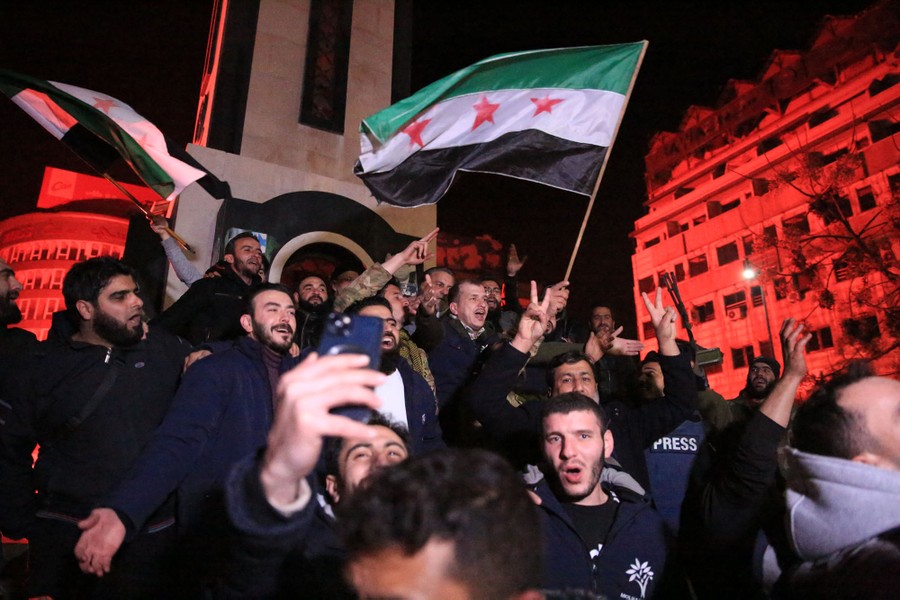 A crowd chants and waves flags in a city square at night.