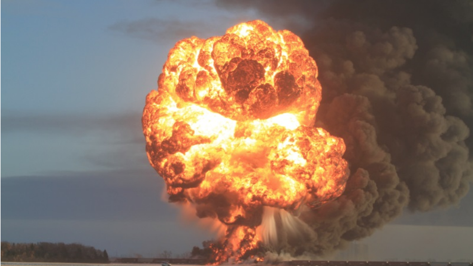 A large fireball and smoke rise from a train on a prairie.