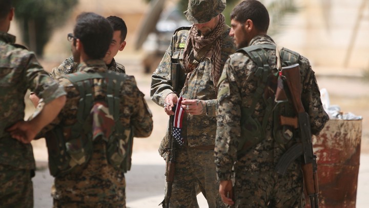 An American fighter carries the American flag as he stands with Syria Democratic Forces (SDF) fighters.
