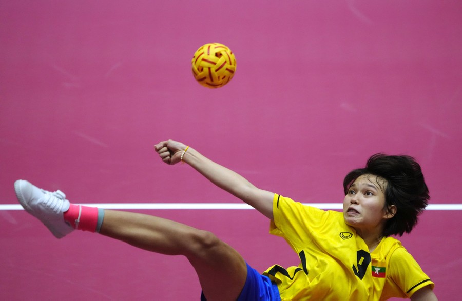 An athlete leaps and twists to kick a small ball above them.