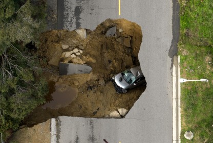 A gray car inside a sinkhole on a roadway