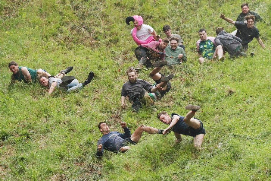 More than a dozen men run and tumble down a steep grassy hill.