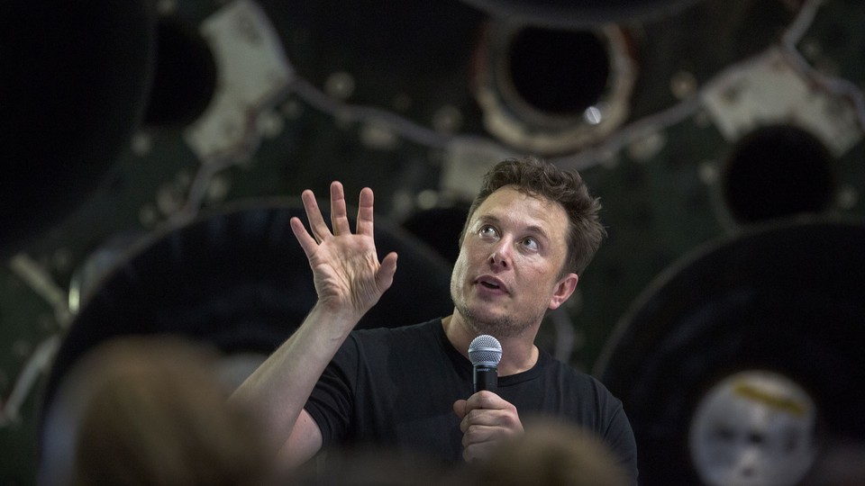 Elon Musk holds a microphone in front of a crowd.