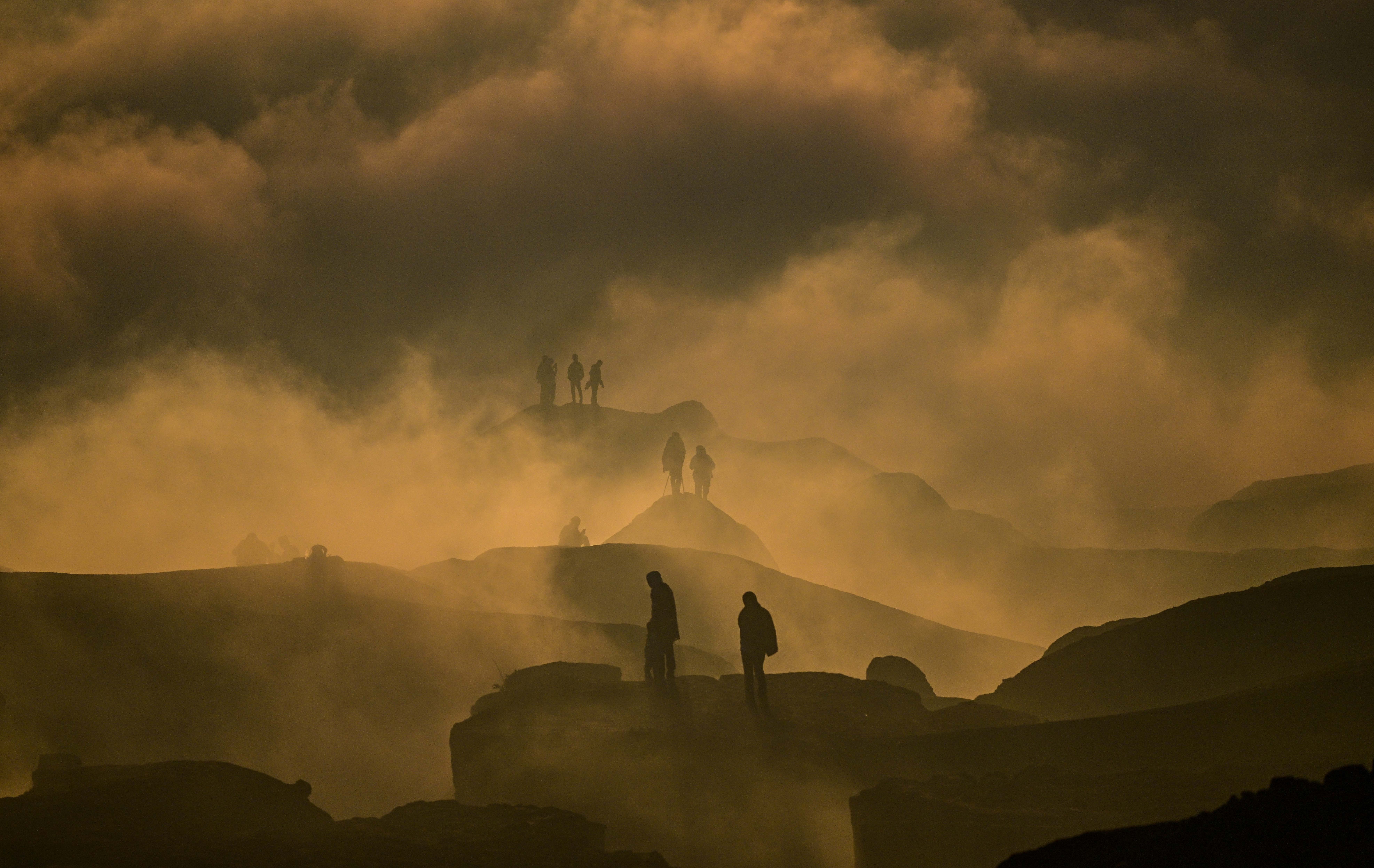 People walk along the rim of a volcano, seen through low-lying clouds.