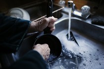 An elderly woman's hands washing a pot in a sink