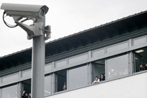 A mounted security camera outside a school with students looking out the window