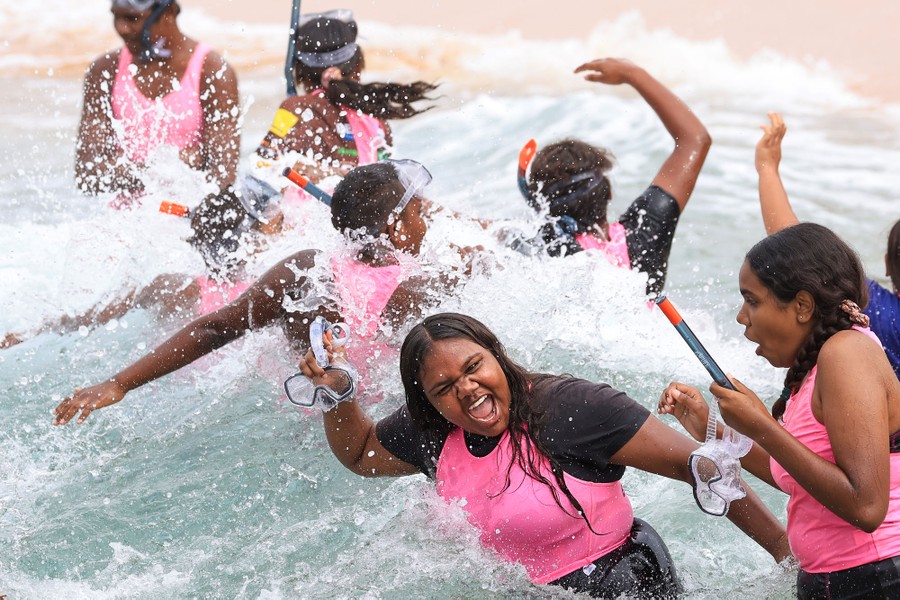 A group of young people play in the surf as a wave passes by.