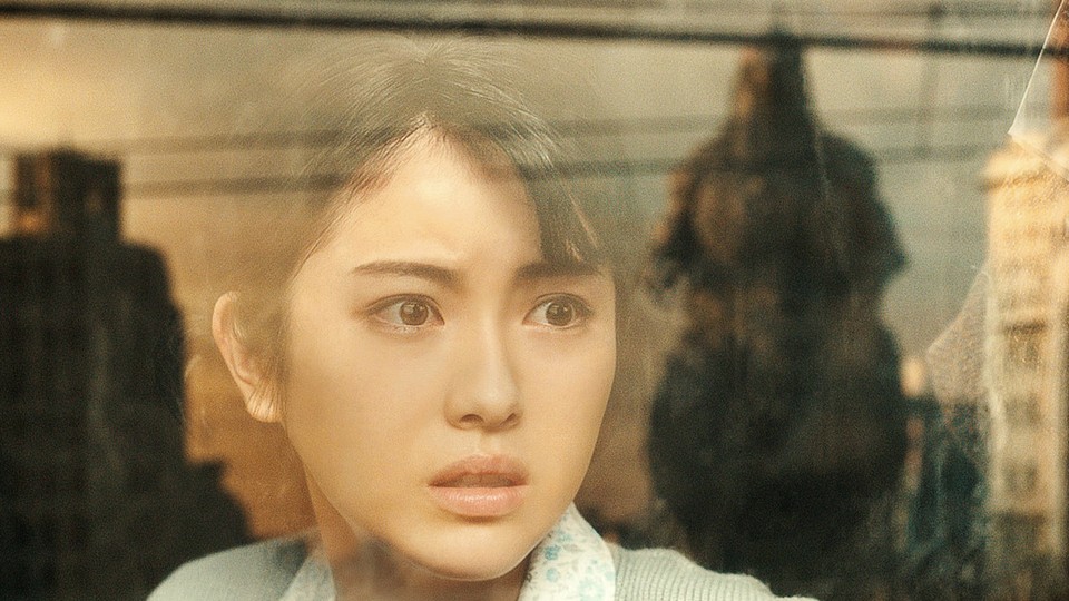 A woman stares at Godzilla through a window