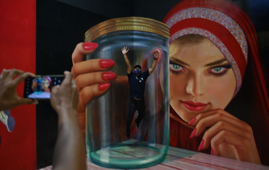A person is photographed in front of a large wall painted to give the illusion of the person being trapped in a huge glass jar.