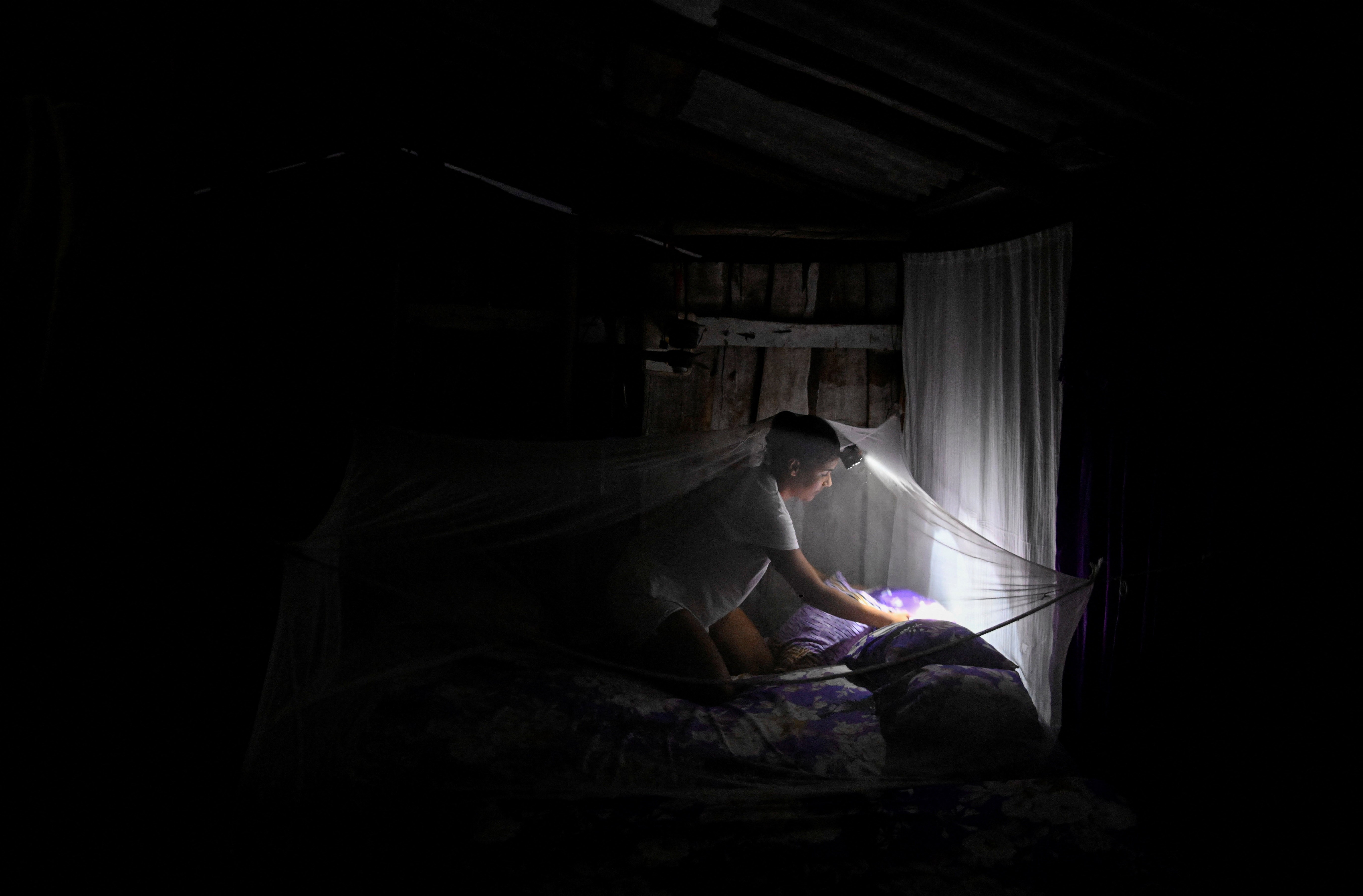 A person uses a headlamp during a blackout while making their bed and arranging a mosquito net.