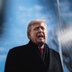 A photo of Trump talking, wearing his winter coat in front of a blurred-out background of a flag pole and bare winter trees
