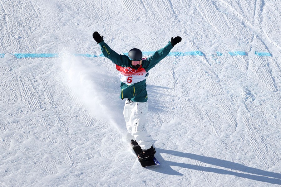A snowboarder raises her arms at the end of a run.